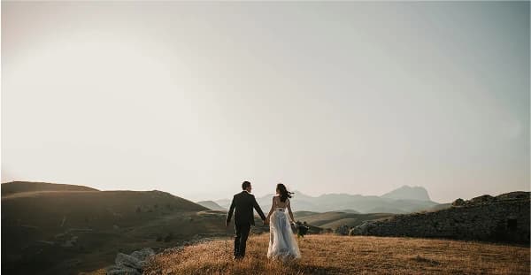 Newlyweds walking through golden hills at sunset