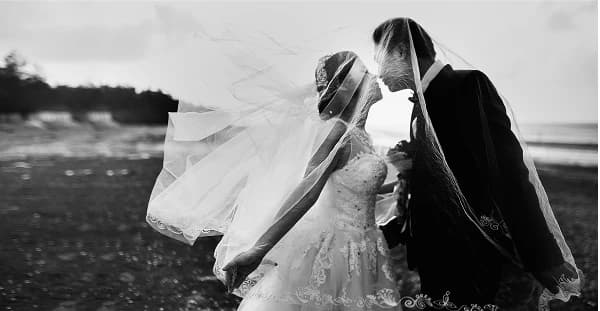 A bride and groom embracing on a windswept coast