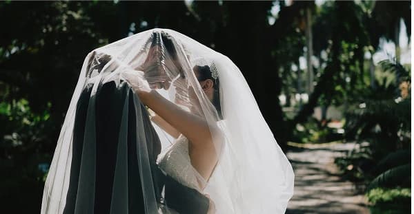 A bride lifting her veil in a sunlit garden