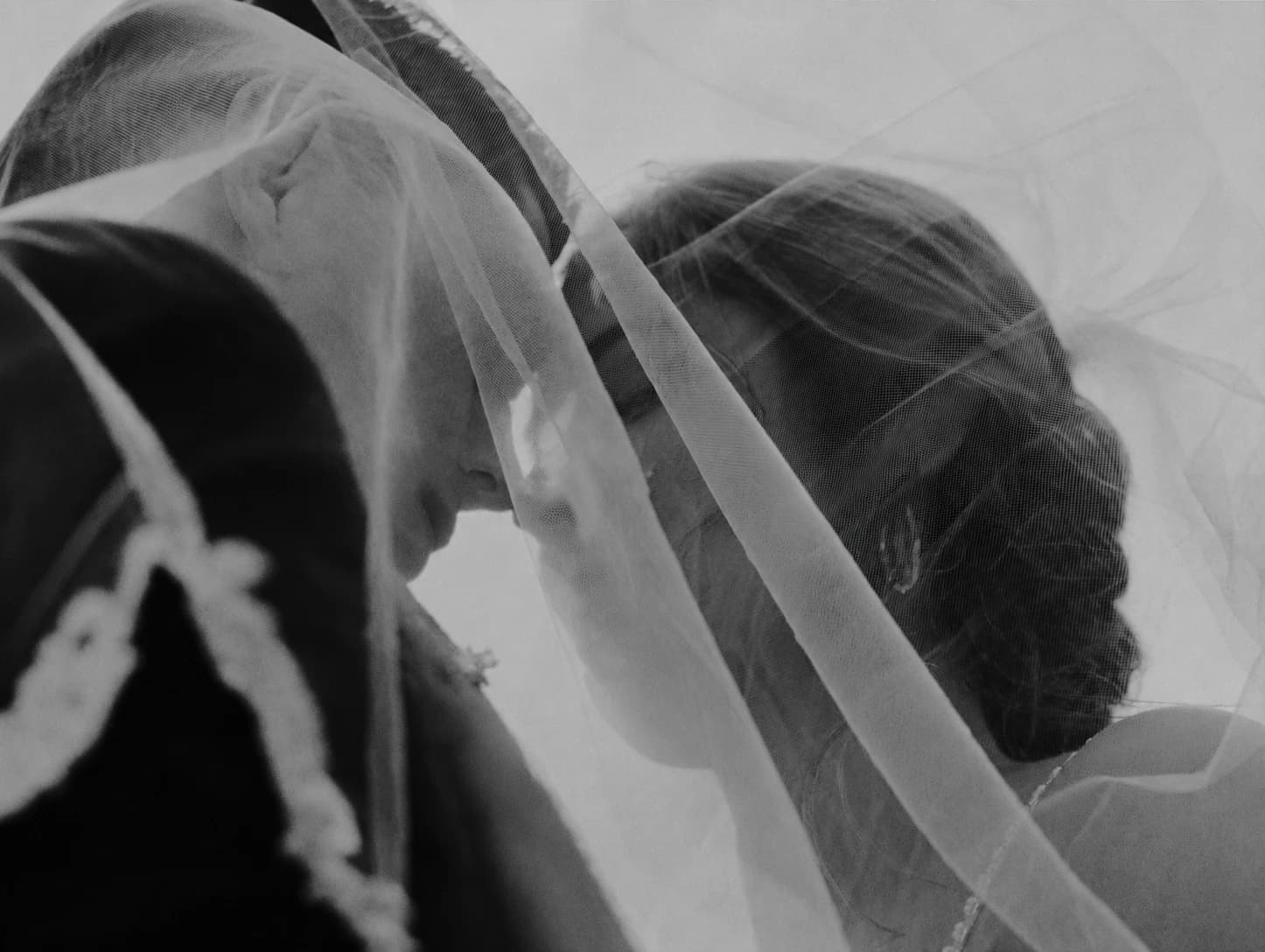 An intimate black and white portrait of a bride and groom beneath a veil